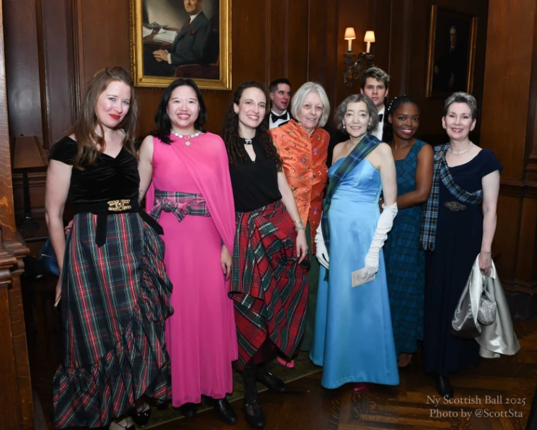 A group of women in evening gowns with tartan skirts and sashes, and two men in black tie, posed in a wood-panelled room at the New York Scottish Ball (2025).