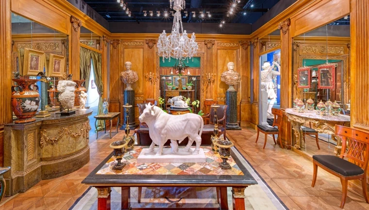 A white marble bull on a specimen-marble table beneath a crystal chandelier, among classical busts and painted urns in a panelled dealer’s stand at a Palm Beach art and antiques fair, at The Palm Beach Show, West Palm Beach, an engagement in the season calendar of The Mansa Court