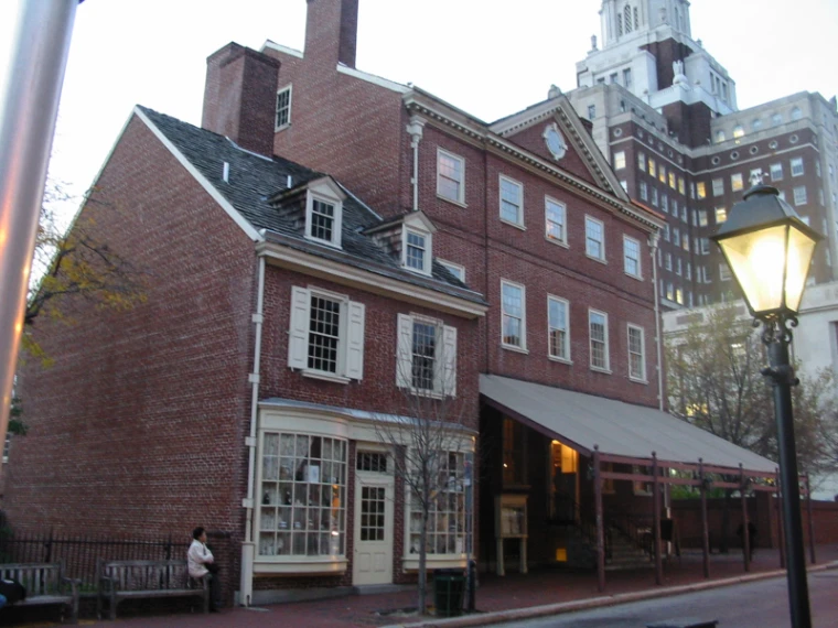 The red-brick front of City Tavern at dusk, an old street lamp lit beside it and bare-branched trees along the pavement (2005).