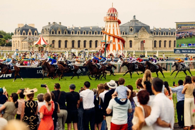 The field racing past the crowd at the rail before the Grandes Écuries of the Château de Chantilly at the Prix de Diane, a mid-June engagement in the season calendar of The Mansa Court