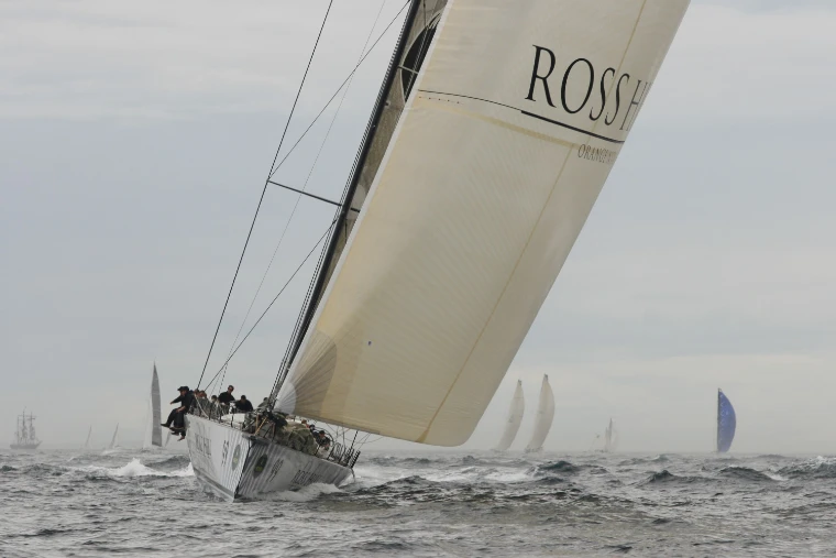 A maxi yacht heeled steeply under a large white mainsail in grey, rough seas off Bondi, its crew on the high side and other yachts behind (2010).