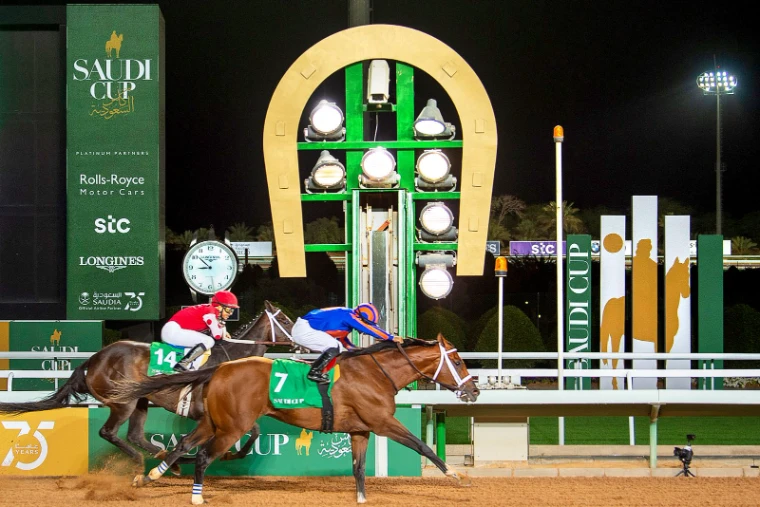 Two horses passing the winning post beneath the golden horseshoe and Longines clock under floodlight at The Saudi Cup, Riyadh, an engagement in the season calendar of The Mansa Court