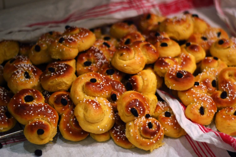 A heap of golden saffron buns, lussekatter, curled into S-shapes and studded with raisins and pearl sugar, on a striped cloth (2009).