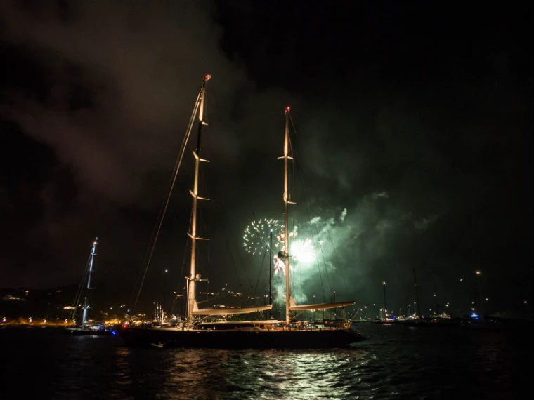 Green fireworks burst at midnight behind the lit masts of a two-masted sailing yacht at anchor off Gustavia, lights reflected in the dark water (2014).