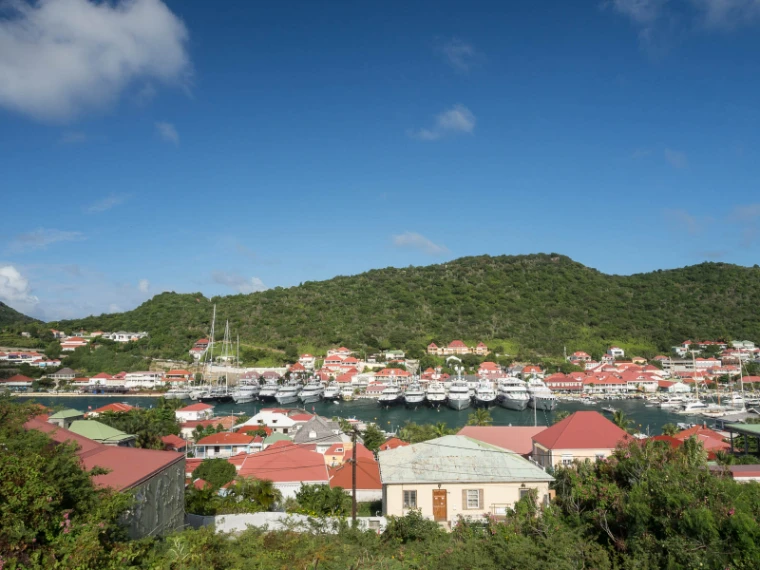 Red-roofed houses of Gustavia seen from the hillside above, the harbour full of white yachts and green hills beyond (2013).
