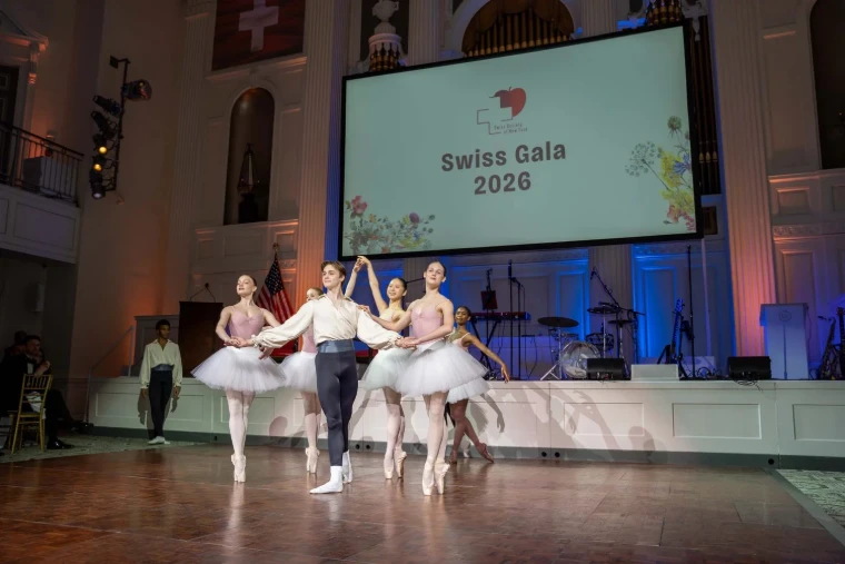 Dancers en pointe performing on stage beneath the Swiss flag at The Swiss Ball, the New York gala, a March engagement in the season calendar of The Mansa Court