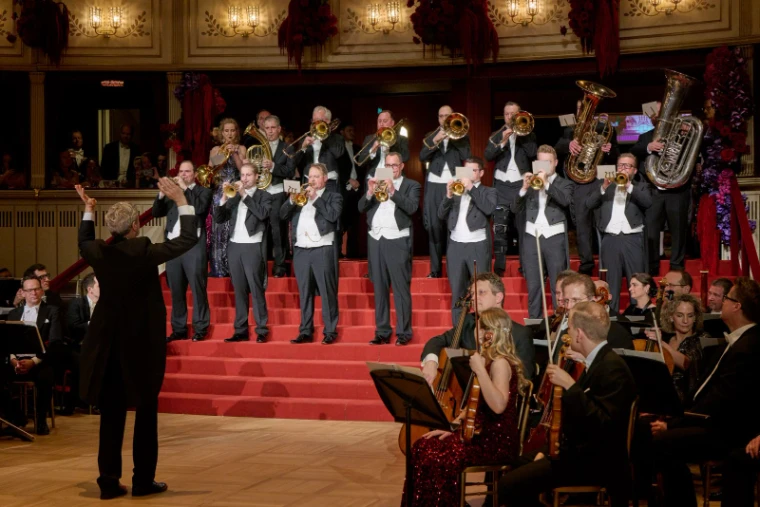 Brass players in white tie sounding the opening fanfare from the red steps above the orchestra at The Vienna Opera Ball, an engagement in the season calendar of The Mansa Court