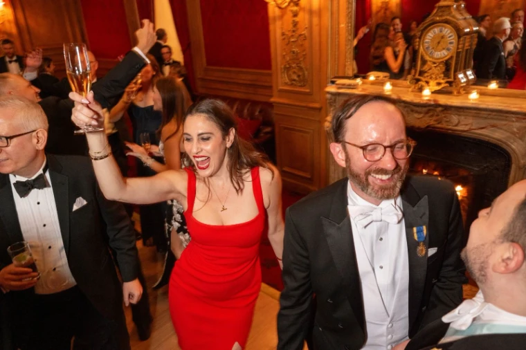Guests dancing with raised champagne before the fire in a panelled crimson room at The Washington Birthday Ball, New York, an engagement in the season calendar of The Mansa Court