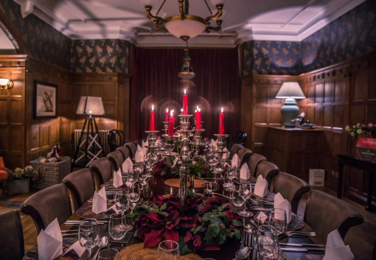 A long dinner table laid with red candles, red flowers and crystal in a dark panelled dining room, for The Winter Table, New York, a winter evening in the season calendar of The Mansa Court