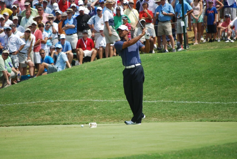 A golfer in a navy shirt follows through on a tee shot as a packed gallery watches from a grassy bank at the 93rd PGA Championship (2011). US PGA Championship, Atlanta Athletic Club, Johns Creek, Georgia, in the season calendar of The Mansa Court