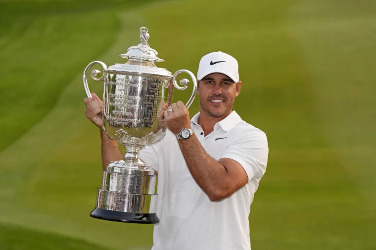 A golfer in white raising the silver Wanamaker Trophy against the green of a fairway, for US PGA Championship, United States in the season calendar of The Mansa Court