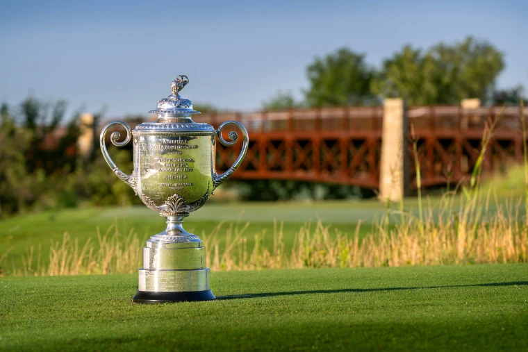 The silver Wanamaker Trophy standing on a tee in low sun, long grass and a timber bridge across the course behind, for US PGA Championship, United States in the season calendar of The Mansa Court
