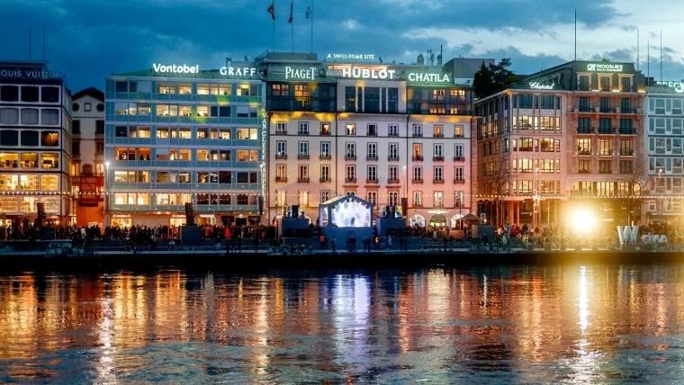 The Geneva lakefront at dusk, its facades lit with the names of the watch houses and a stage set on the quay, during the week of Watches and Wonders, an early-April engagement in the season calendar of The Mansa Court